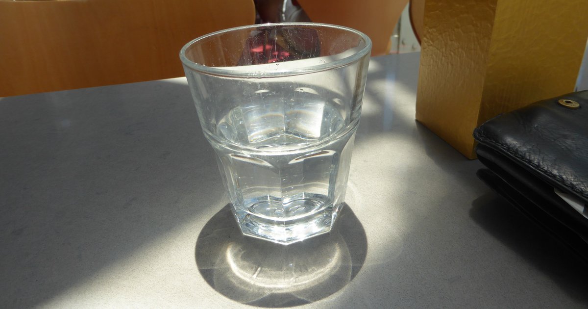 A glass of water sitting on a table, half filled