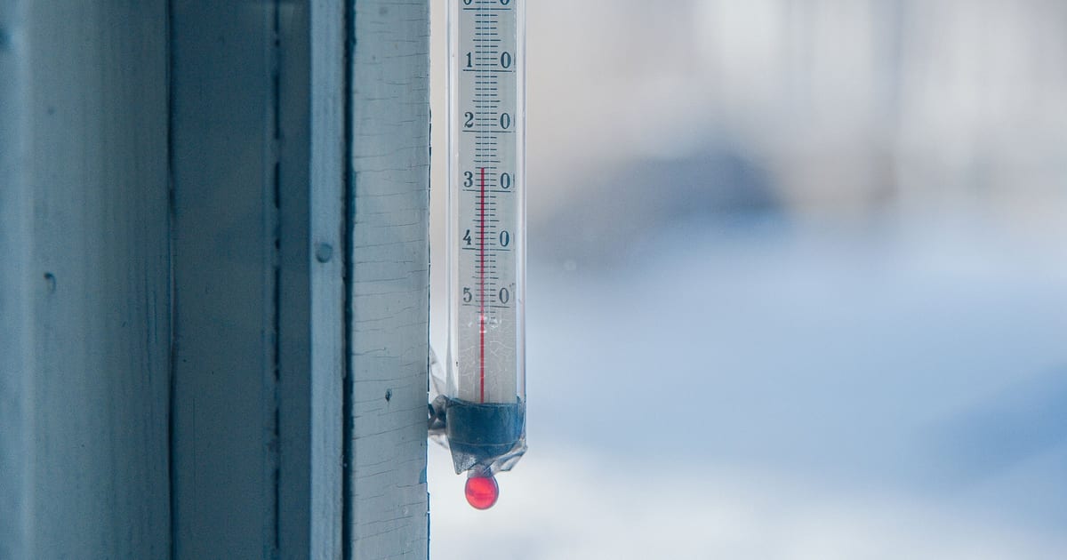 An outdoor thermometer fixed to a window frame, with snow blurred in the background
