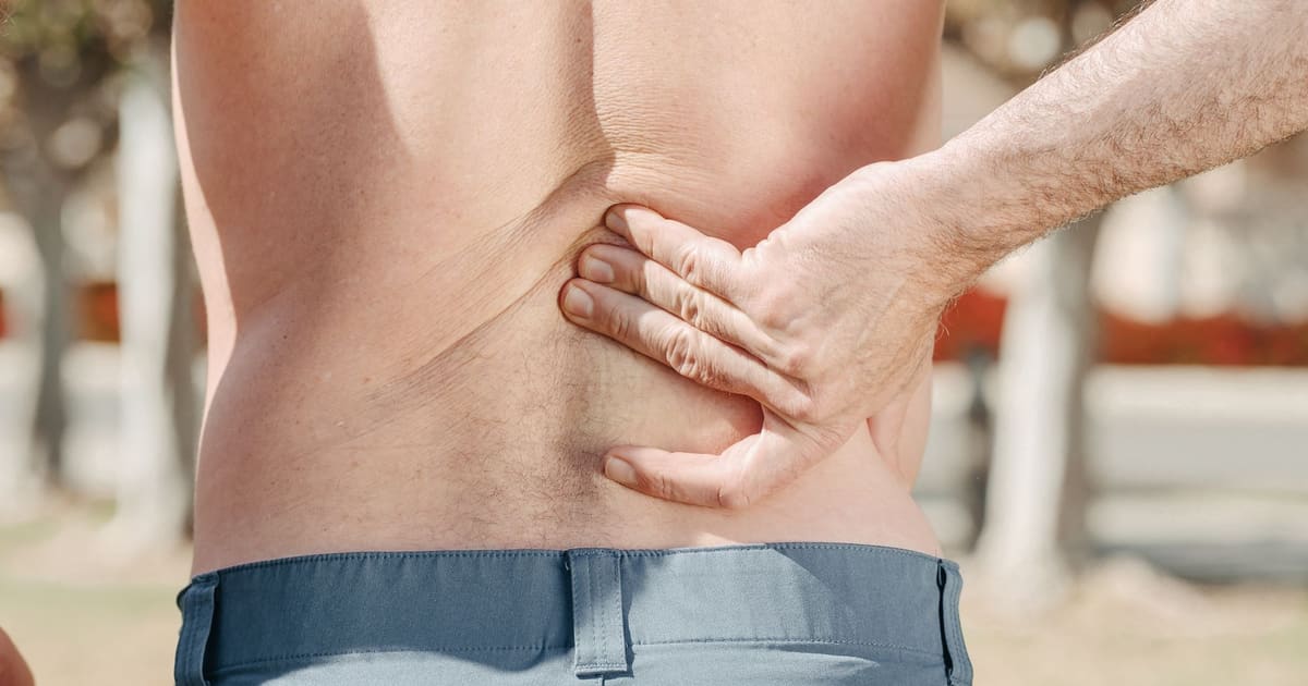 Close-up of a man pressing one hand against his lower back, seen from behind