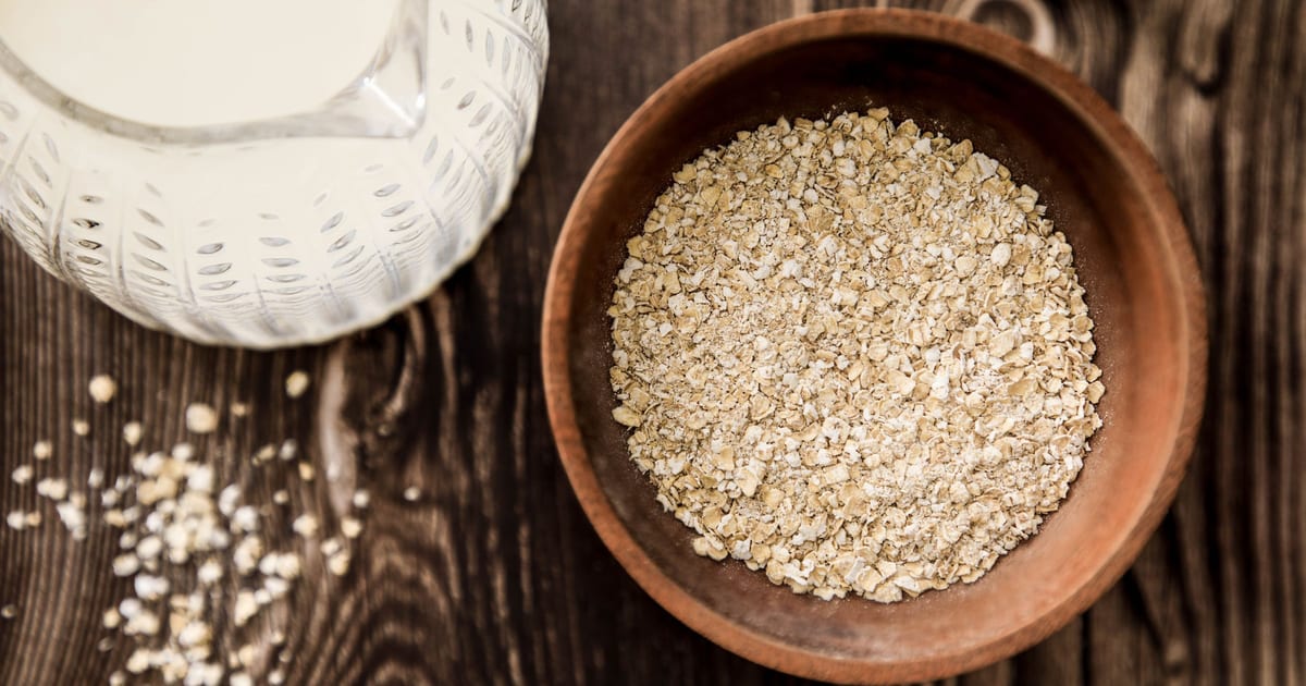 A wooden bowl of rolled oats next to a glass jug of milk on a dark wooden table