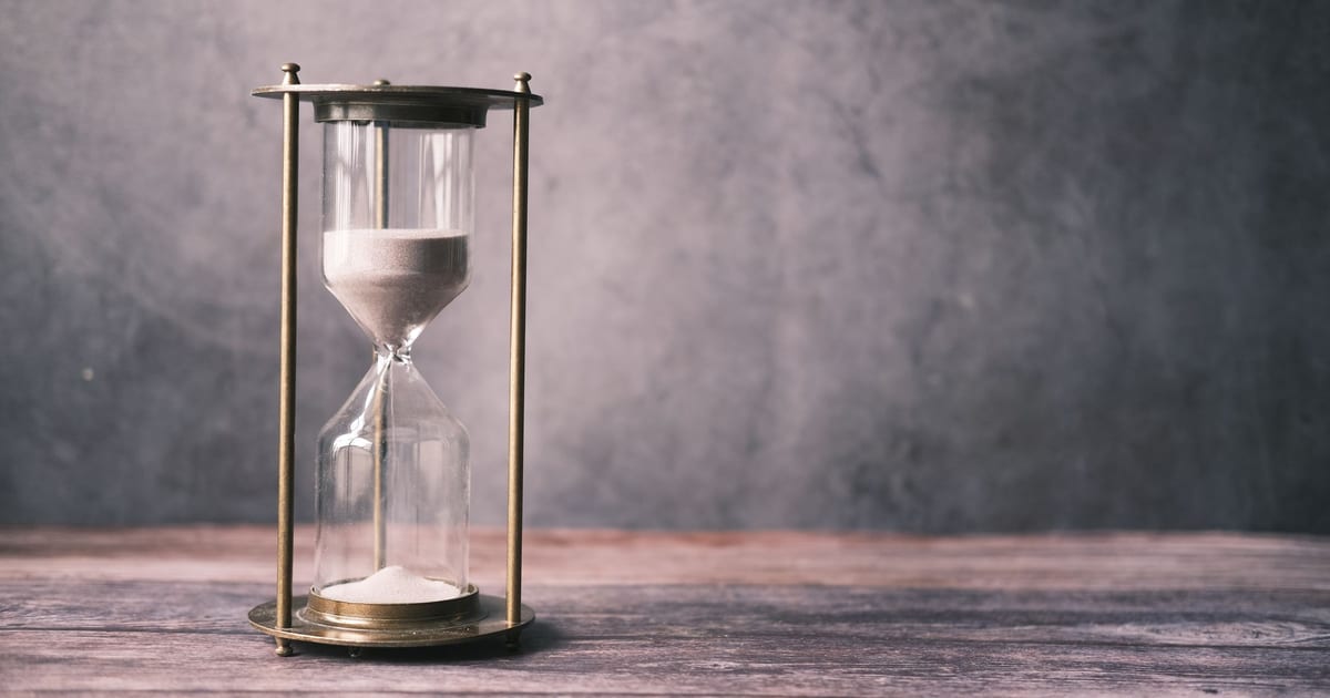 An antique brass hourglass with sand running on a wooden table