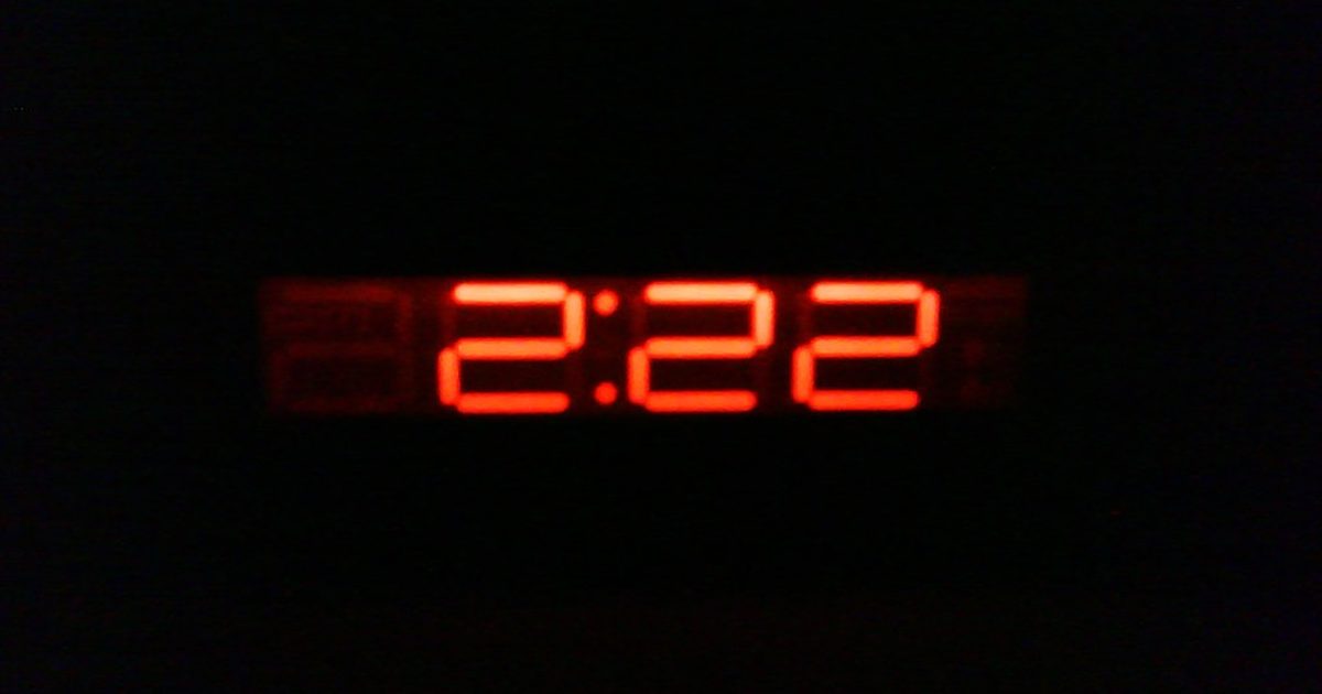 A digital clock glowing red in a dark room, reading 2:22
