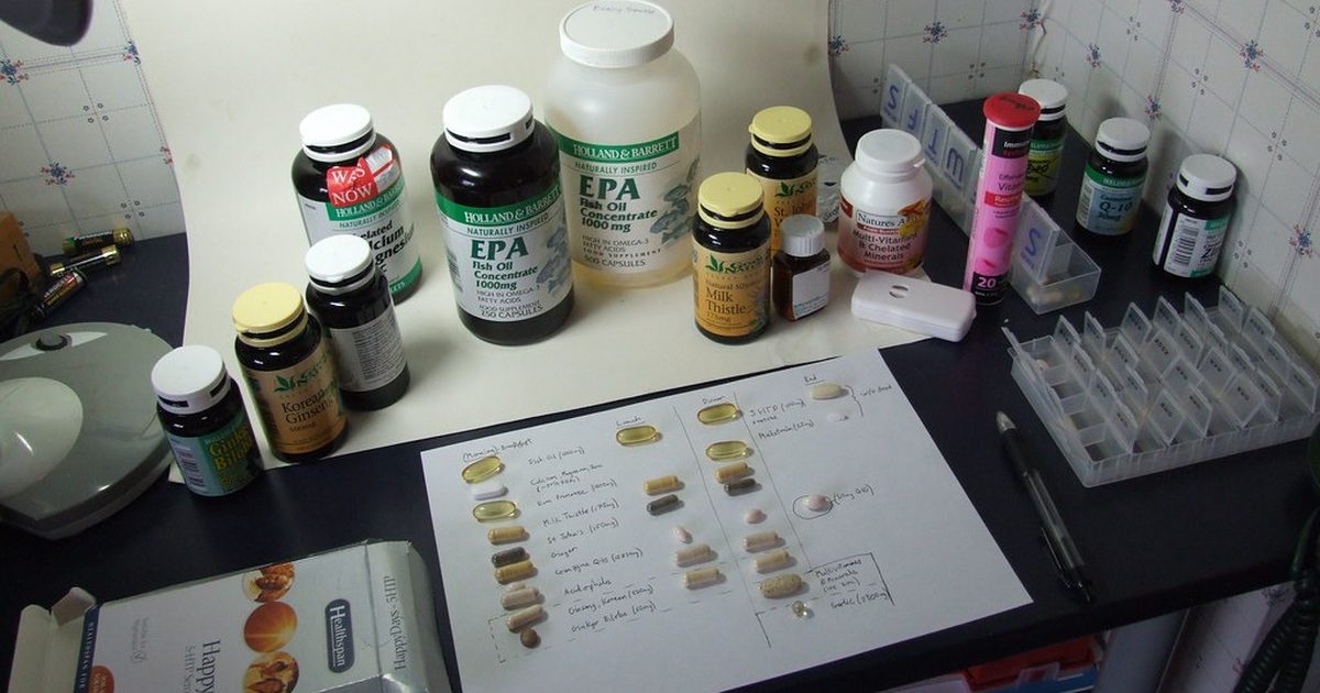 Supplement bottles on a desk beside a handwritten chart listing each capsule and its amount