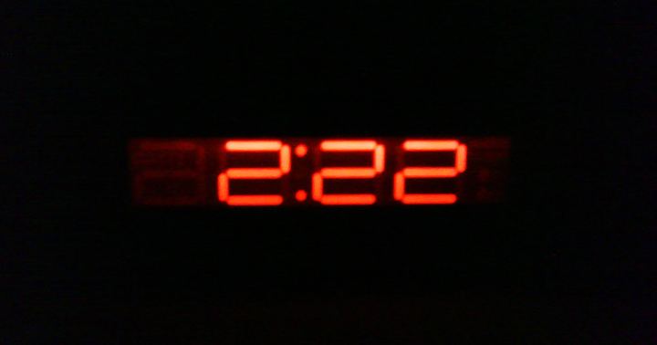 A red digital bedside clock reading 2:22 in a dark room