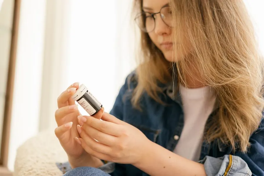 Person carefully reading the label on a supplement bottle before taking it