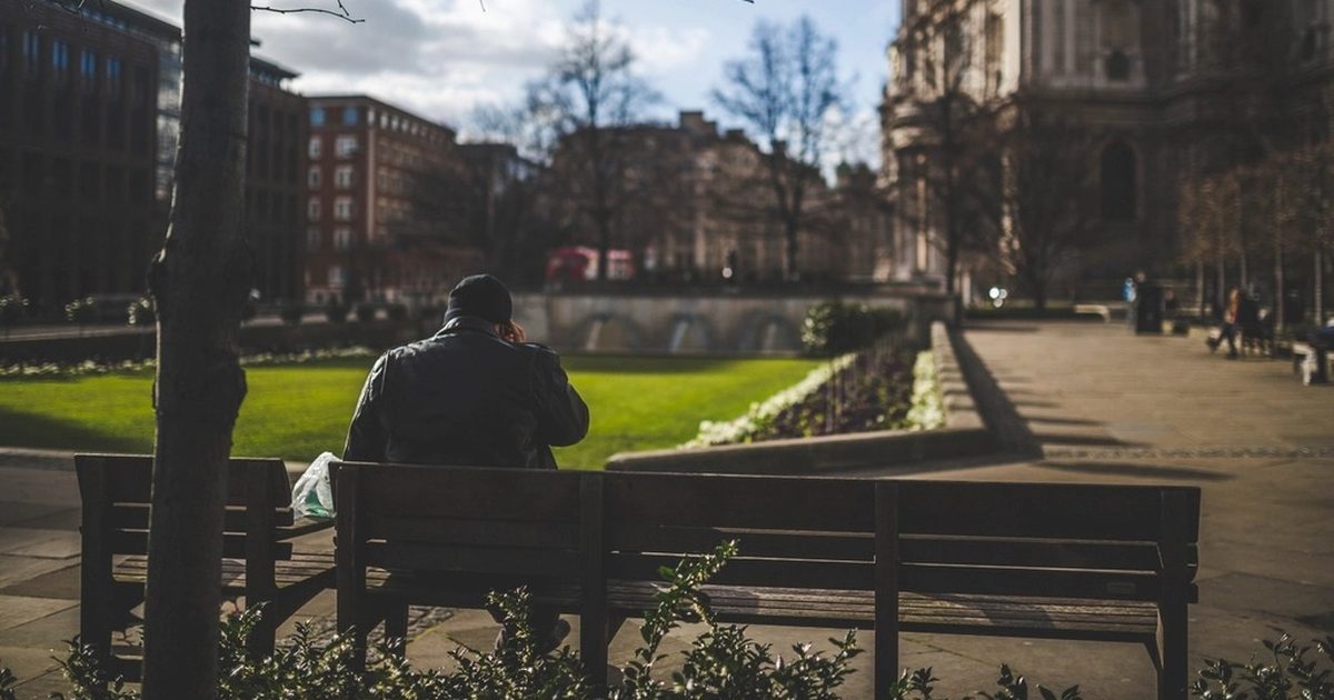 A man in a dark jacket sitting alone on a park bench, seen from behind