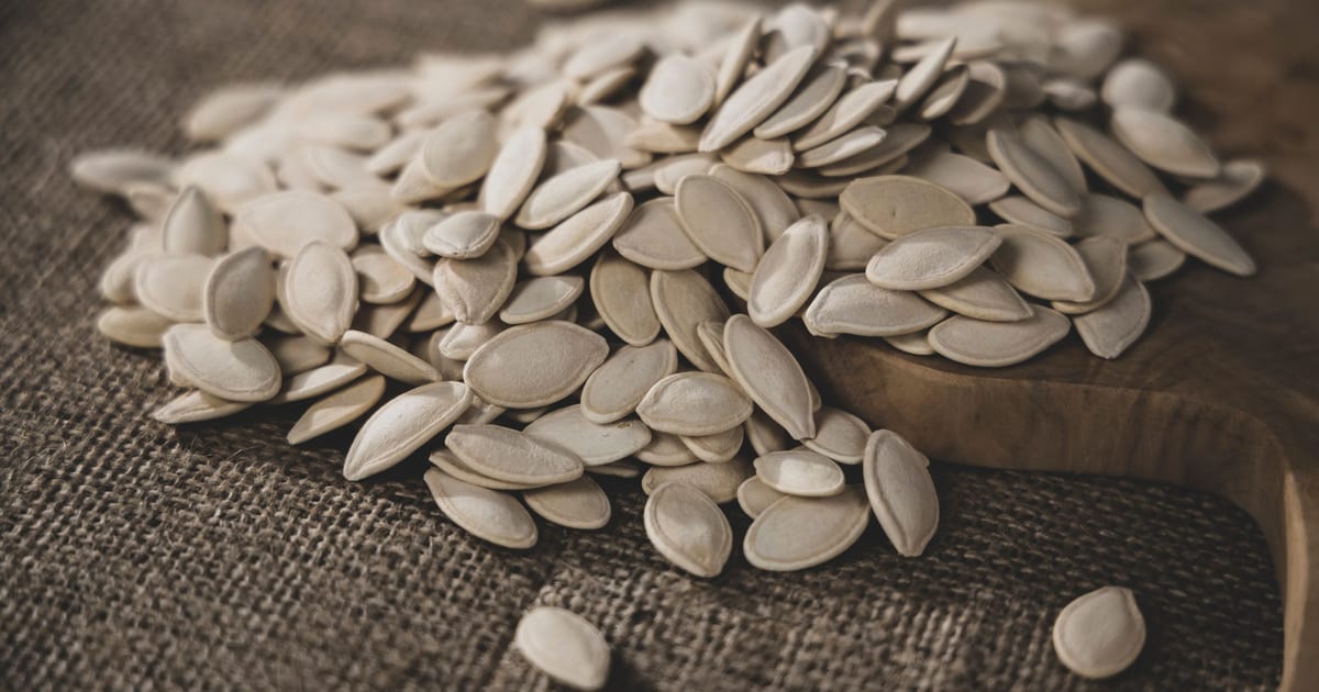 A pile of whole pumpkin seeds in the shell on burlap and a wooden board