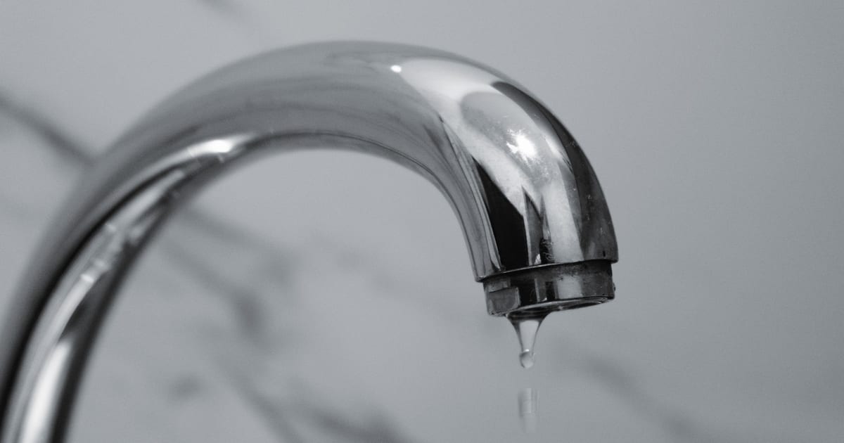 A chrome bathroom faucet with a single drop of water falling from the tip